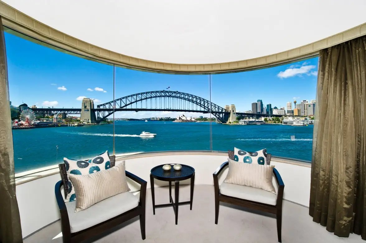 Lounge behind curved floor-to-ceiling windows, with the Harbour Bridge beyond